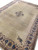 Angled view of oversized wool rug with blue palmette border and plain golden field