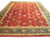 Angled studio view of red Persian Tabriz rug with emerald green floral border and ivory guards