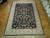 Angled view of traditional black area rug with cream floral border and sage guard stripes