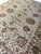 Angled close-up of all-over floral field showing taupe palmettes, green leaves and ivory wool pile