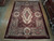 9'6" x 13'6" Chinese Savonnerie rug displayed flat on a wood showroom floor