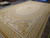 Mansion size Aubusson rug displayed on warehouse floor showing ivory field and gold ribbon borders