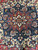 Detail of indigo medallion lobes framed by golden ivory ground and multicolored blossoms in soft wool
