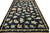 Oversize black needlepoint area rug angled view with tan ribbon and rosette border framing floral field