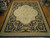 Overhead showroom photograph of black and gold Aubusson rug laid flat across parquet flooring