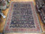 11'2" x 14'2" Persian Mahal rug laid flat on showroom parquet floor beside stacked rugs