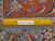 Ruler placed on brick red border measuring the fine hand-knotted wool pile and weave