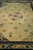 Lengthwise view showing central medallion, floral sprays and the navy Greek key inner border of the beige rug