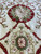 Detail of a red rimmed rosette with sage petals over creamy ivory wool ground