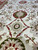 Close view of burgundy medallion flower above ivory diamond cartouche on cream ground