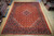 10x13 Persian Tabriz rug shown on warehouse wood floor beside rolled Oriental rugs for scale