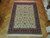 Rug laid out on parquet flooring, pale field and red border seen from above with fringe in foreground