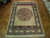Rug laid flat on herringbone parquet, whole design visible with fringed ends and pale wide border