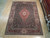 Hand-knotted 8'7" x 11'9" Sino Tabriz rug displayed on showroom hardwood floor beside rolled rug inventory