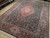 Angled showroom view showing dark green all-over floral field, berry red border, ivory corner cartouches