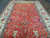 Hand-knotted wool rug seen lengthwise, coral field framed by ivory border with red rosettes