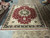 Showroom view of 12 by 15 hand-knotted rug with red field and ivory spandrels