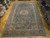 10' x 16' Tabriz rug displayed on parquet floor surrounded by rolled Persian rugs in showroom