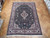 Hand-knotted wool rug on parquet floor showing ivory main border and dark floral medallion center