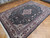 8x12 Sino Tabriz rug angled on wood floor, deep black field with rose and salmon blossoms
