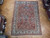 Overhead view of coral and ivory hand-knotted Tabriz rug among rolled Persian rugs