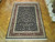 Black and burgundy hand-knotted wool rug shown on parquet floor with all-over floral vine field