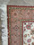 Close-up corner showing salmon pink border, red guard stripes and thick ivory cotton fringe