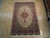 Hand-knotted 6 x 10 wool rug laid on light hardwood showroom floor, fringe fully visible