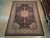 8'6" x 11'6" hand-knotted Oriental rug displayed on light wood showroom floor beside rolled rugs
