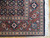 Corner detail showing rust floral border, ivory guard stripes and hand-tied cotton fringe