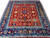 Near square 7x8 Oriental rug showing red field, navy main border and light blue guard bands