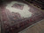 Angled view of vintage ivory Sarough rug showing wine red border, fringe and wool pile