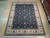 9'2" x 12'3" Oriental rug displayed on light wood showroom floor beside rolled rug stacks
