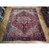 Semi-antique 9'8" x 12'4" Heriz rug displayed on parquet showroom floor beside stacked rugs