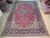 10' x 15'5" Persian rug displayed on showroom floor beside stacked handmade Oriental rugs