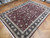 Angled view of burgundy and black hand-knotted area rug with ivory fringe on wood flooring