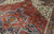 Wool pile texture across the madder red field, angular leaves and indigo medallion framing