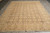 Hand-knotted wool rug displayed on gray floor showing taupe field, gold blossoms and wide geometric border