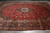 Angled view of the red wool rug showing navy corner spandrels and five layered floral borders