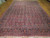 Oversize hand-knotted wool rug seen lengthwise, navy border framing a dense raspberry red floral repeat