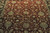 Close-up of sage green and gold palmettes woven across the deep burgundy wool field
