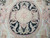 Close view of the oval medallion, plaited ribbon, rosette centre and small woven lyres