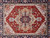 Ivory corner spandrels with hooked vines beside the red field of this wool area rug