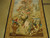 Angled view of scenery wall hanging with sage green urn, blossoming bouquet and golden acanthus border