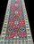 5'3" x 24' Pakistani Kazak runner showing repeating navy diamond medallions on a red field