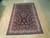 6'10" x 10'7" Sarouk rug displayed on light wood floor showing navy field and rose border