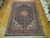 Hand-knotted wool rug on parquet floor showing rust red border and dense navy floral field