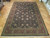 Large hand-knotted Oriental rug displayed on parquet showroom floor, black field framed by burgundy floral border