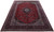9'9" x 13'7" Persian Kashan rug photographed at an angle, deep red field, navy floral border