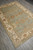 Angled view of 6x9 hand-knotted Oushak area rug on gray wood floor, soft blue field